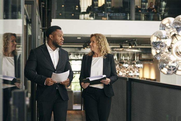 Male and female law experts holding documents talking with each other while walking in office corridor
