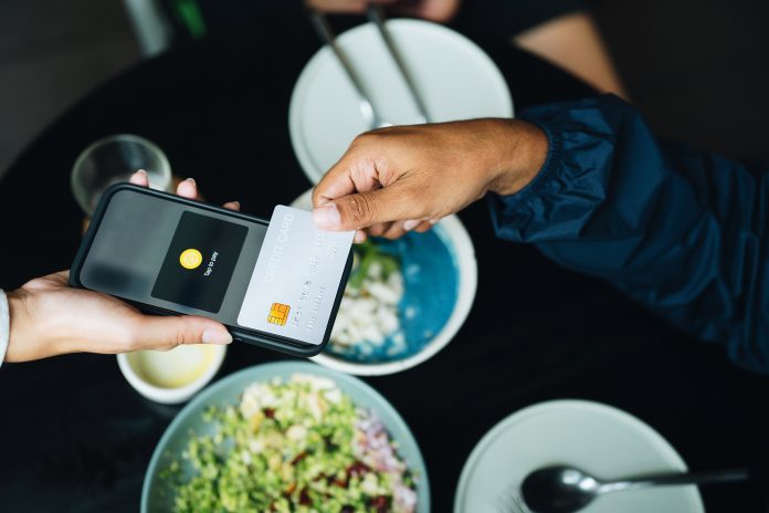 Close-up shot of man tapping a credit card on a smartphone to make a contactless payment at an organic healthy restaurant